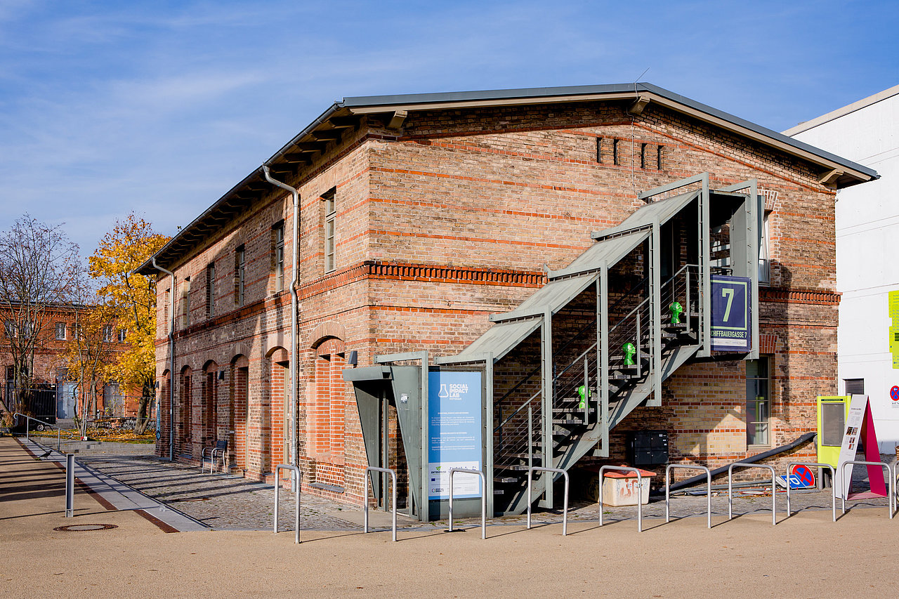 Zweistöckiges Backsteingebäude. Außen führt eine Treppe in das 1. Obergeschoss.