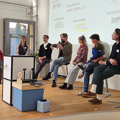 Die Paneldiskussion auf der Bühne findet statt mit Thorsten Jahnke von der Social Impact gGmbH / Kompetenzzentrum für Soziales Unternehmertum, Julia Paaß vom Netzwerk Zukunftsorte, Frederik Fischer von Neulandia, Tobias Kremkau von CoWorkLand eG, Petra Liesenfeld vom Bahnhof Klasdorf, Adrian Schefer des Marktplatz Waldschänke GmbH und Christian Berkes von der Präsenzstelle Luckenwalde
